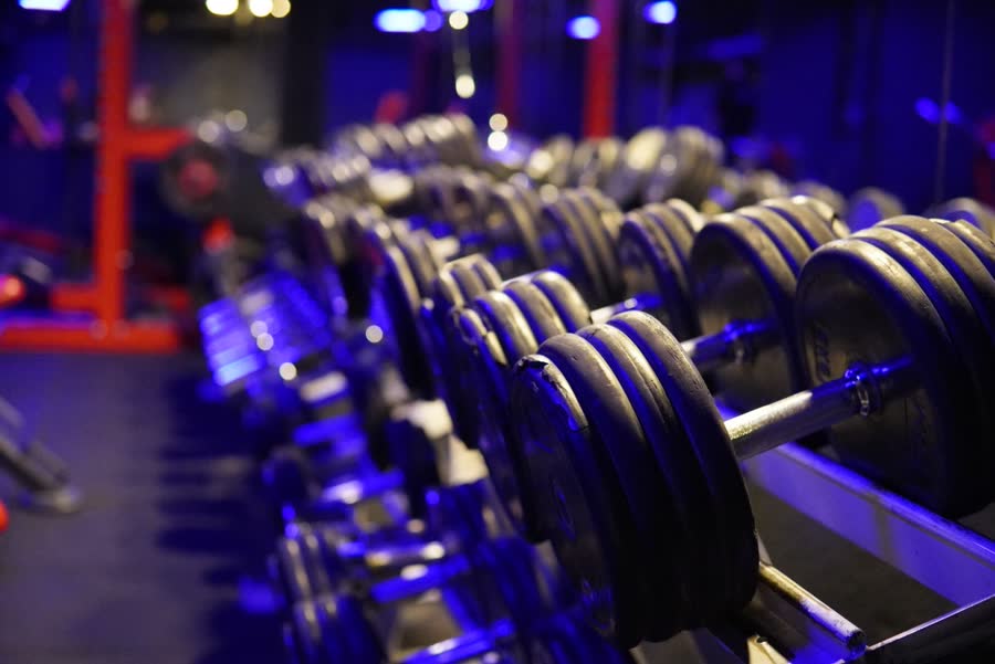 Long rack d'haltères éclairé en bleu, machines rouges en arrière-plan