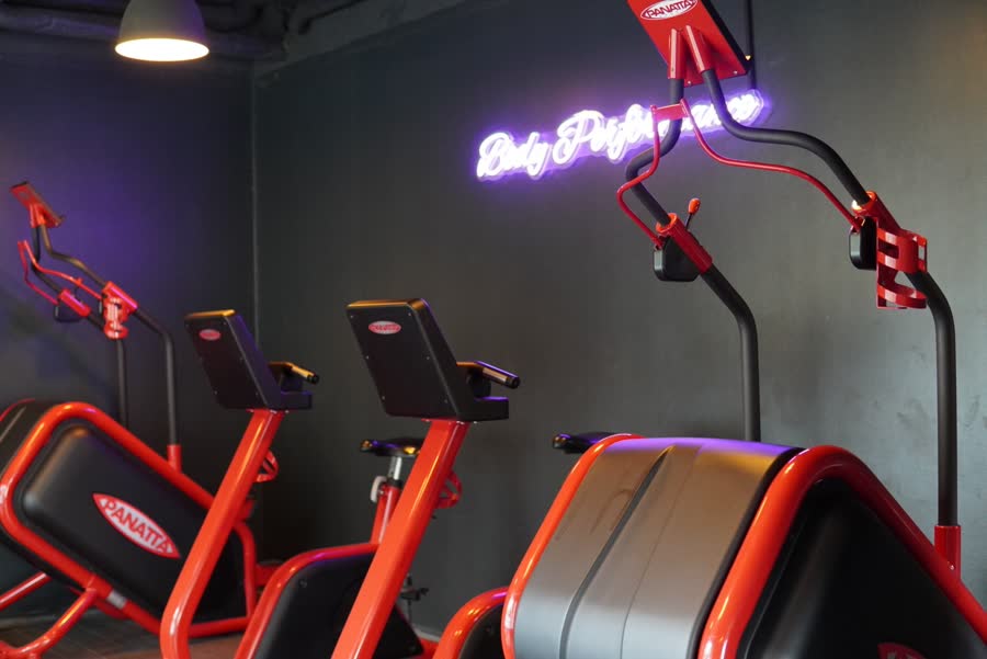 Espace cardio : machines rouges et noires sous l'enseigne néon violette Body Performance