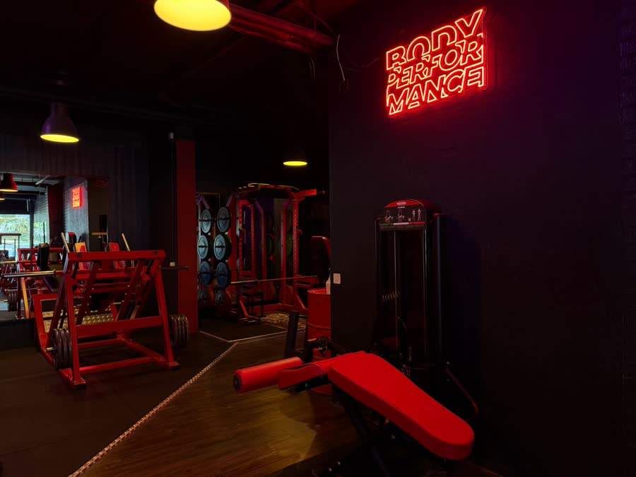 Néon rouge Body Performance au mur, machines pour les jambes et banc rouge au premier plan